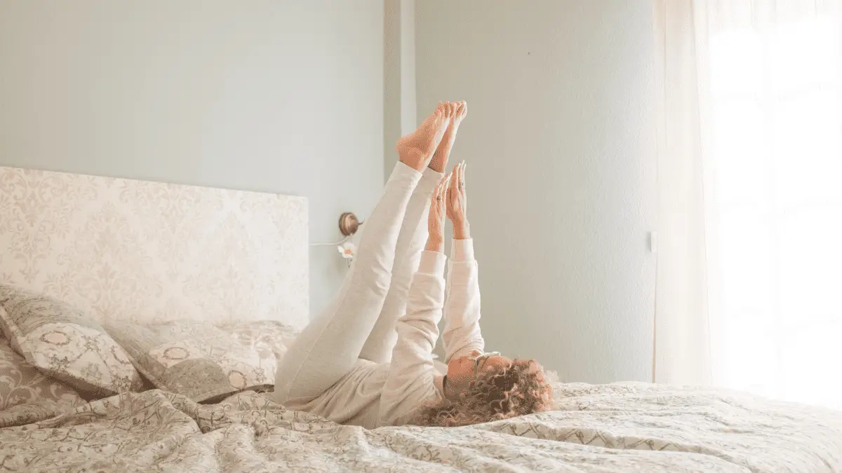 A person performing leg raises on a bed, showcasing a simple yet effective ab exercise. Elevate your legs to engage your core muscles, promoting a flat stomach even in the comfort of your bed